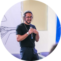 Homem sorridente de camiseta preta segurando um microfone durante uma apresentação.