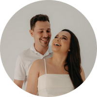 Casal sorridente, homem atrás da mulher que ri com a cabeça levemente inclinada para trás.